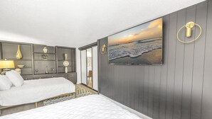 A bedroom with two beds, a large wall-mounted TV, and a view of the ocean. - Gertrude's Siesta | Bayview Unit w/ Balcony, Pools & Private Beach (Sarasota)