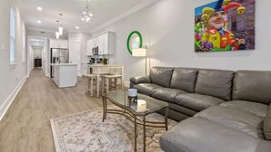 Ein modernes Wohnzimmer mit Ledersofa, Glastisch und einer Küche im Hintergrund.