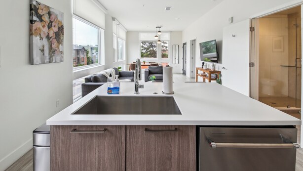 A modern kitchen with a central island, stainless steel appliances, and a large window providing a view of the cityscape. - Highline Hideaway | Corner 1BR LoHi Loft | Quiet | Dog-Friendly (Denver)