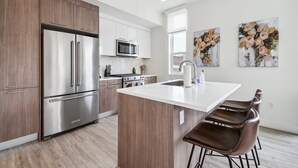A modern kitchen with stainless steel appliances, a central island with bar stools, and artwork on the walls. - Highline Hideaway | Corner 1BR LoHi Loft | Quiet | Dog-Friendly (Denver)
