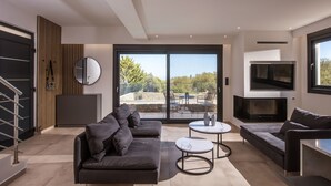 Ein modernes Wohnzimmer mit einer Couch, zwei Couchtischen, einem Fernseher und einem Balkon mit Gartenmöbeln.