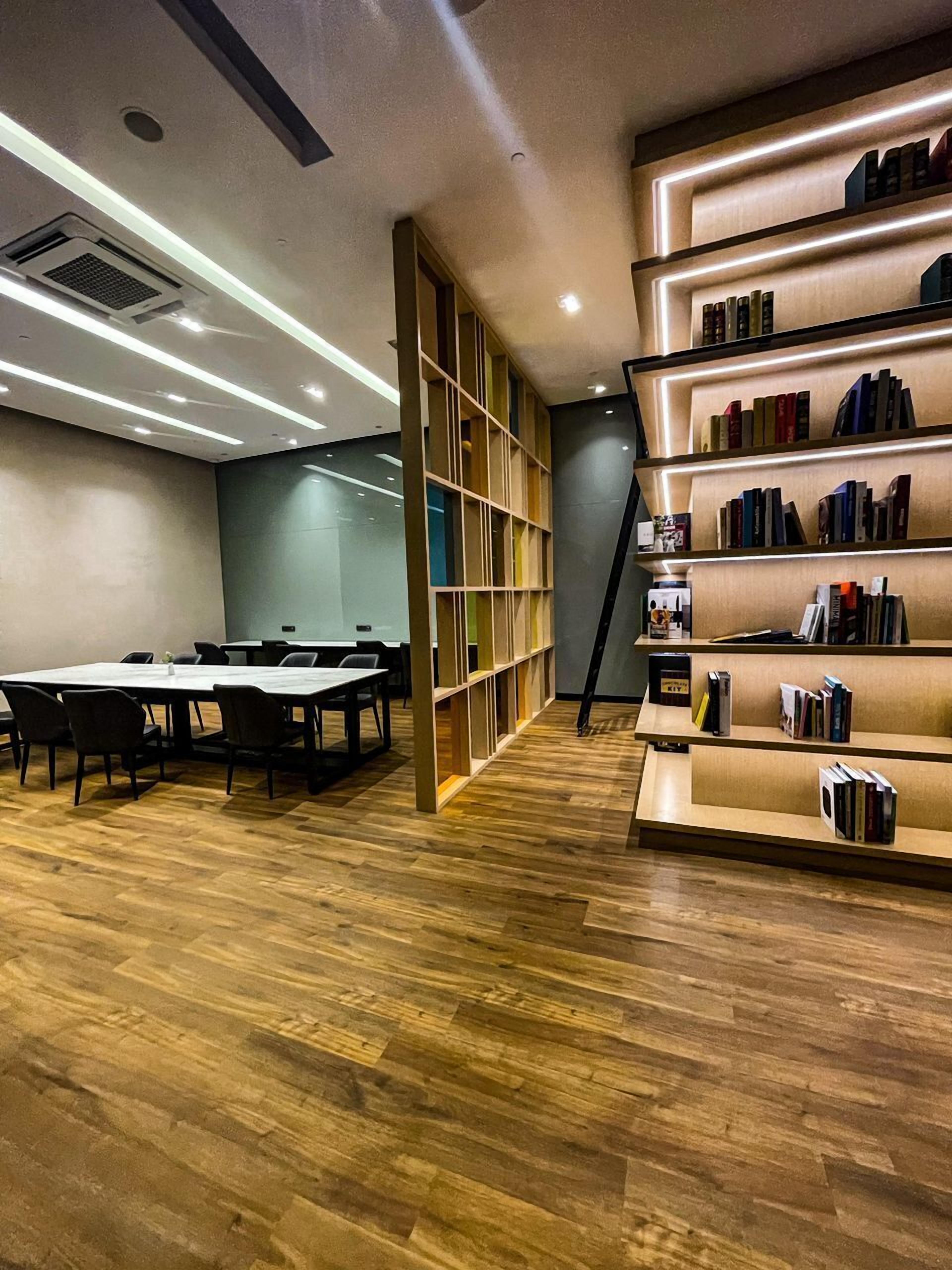 A modern conference room with a long table and chairs, a bookshelf with books, and a wooden floor.