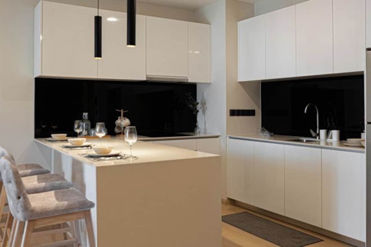 Una cocina moderna con armarios blancos, una isla central con asientos e iluminación colgante.