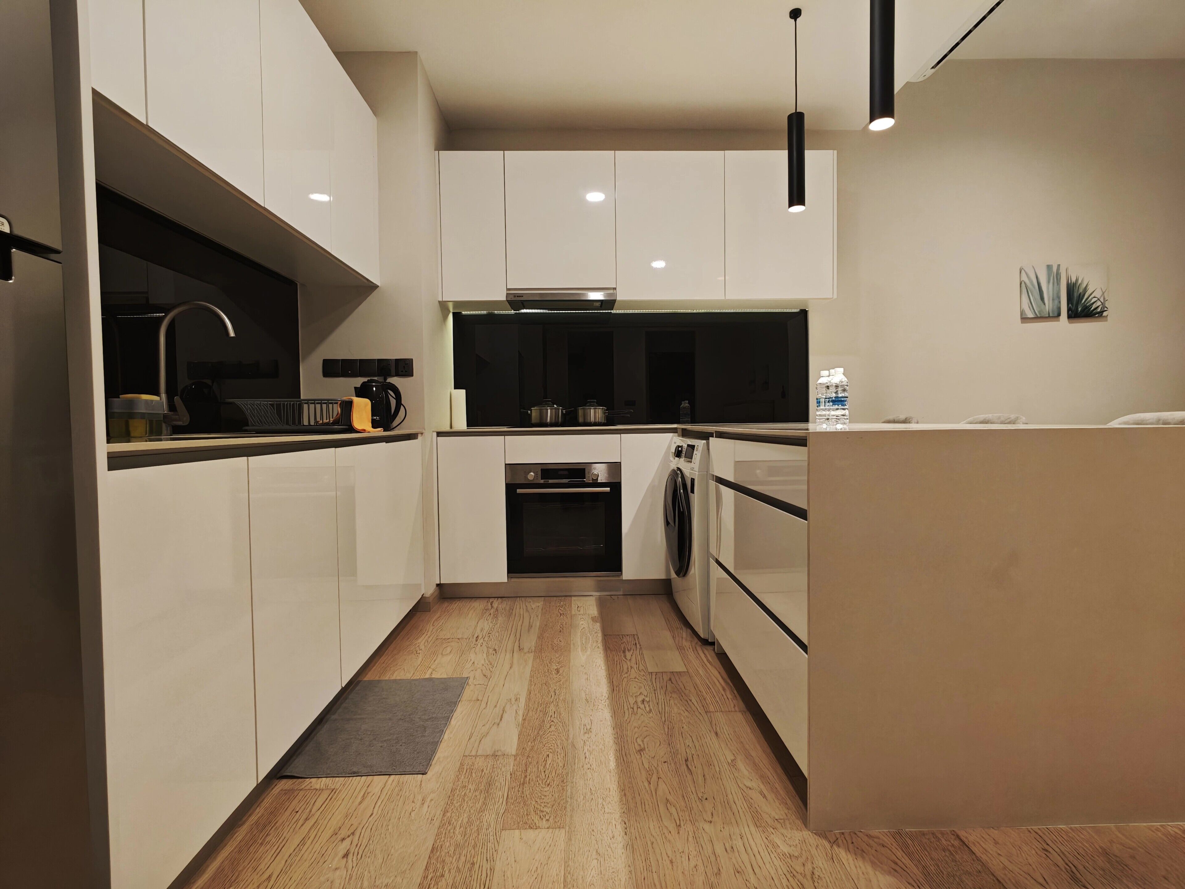 A modern kitchen with white cabinetry, a built-in oven, a washing machine, and a coffee maker.