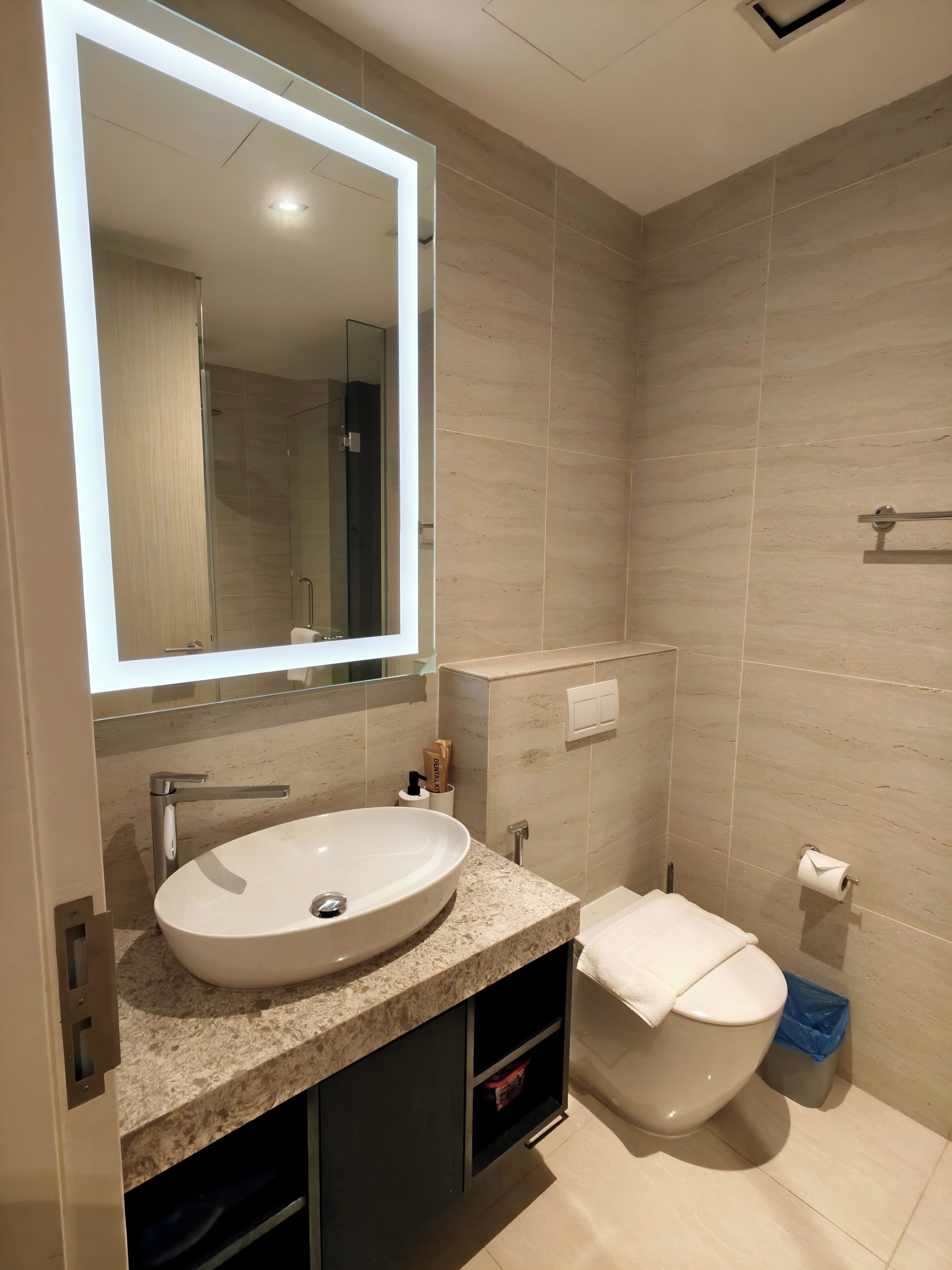 A modern bathroom with a large mirror, a sink, a toilet, and a shower.