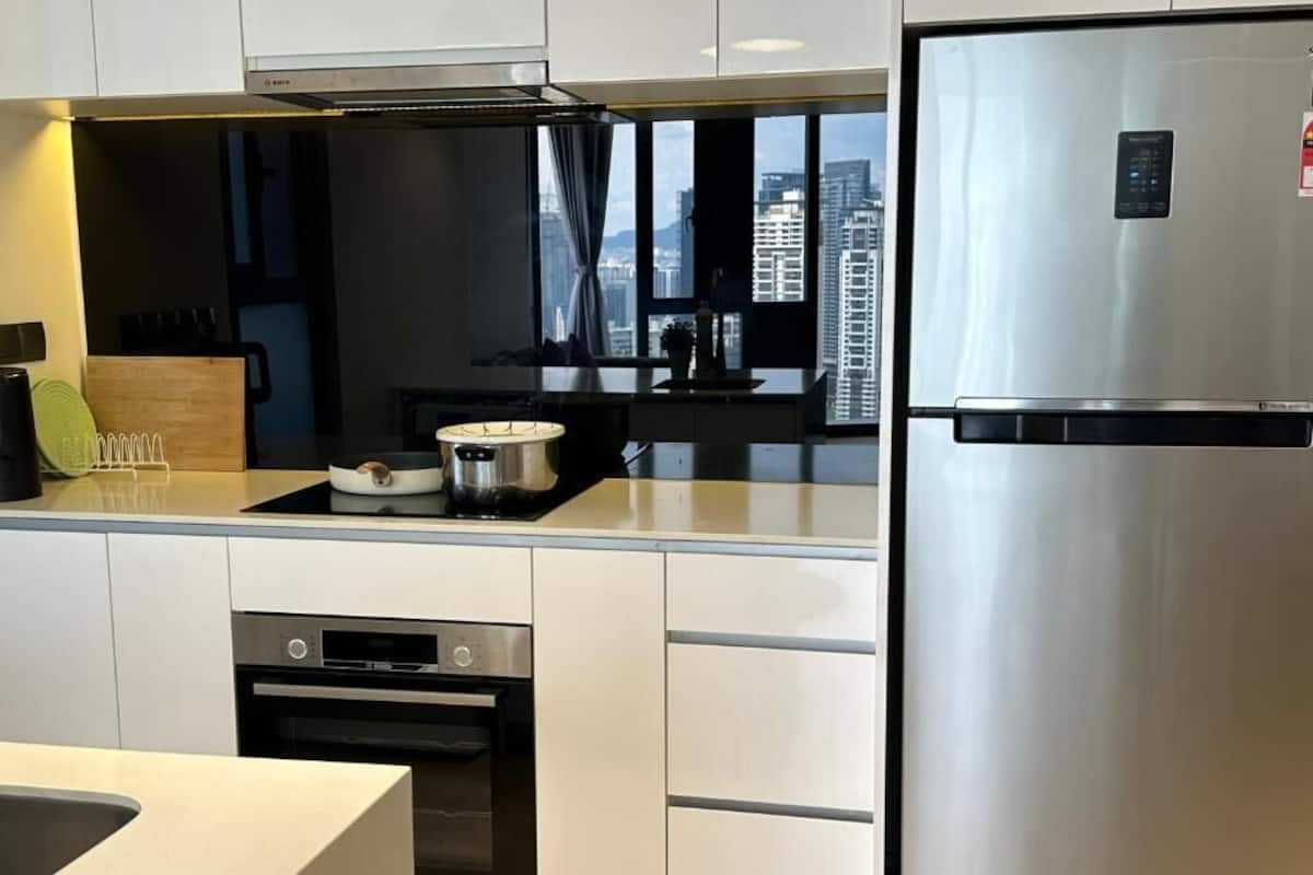 A modern kitchen with white cabinets, a stainless steel refrigerator, and a view of the cityscape through large windows.