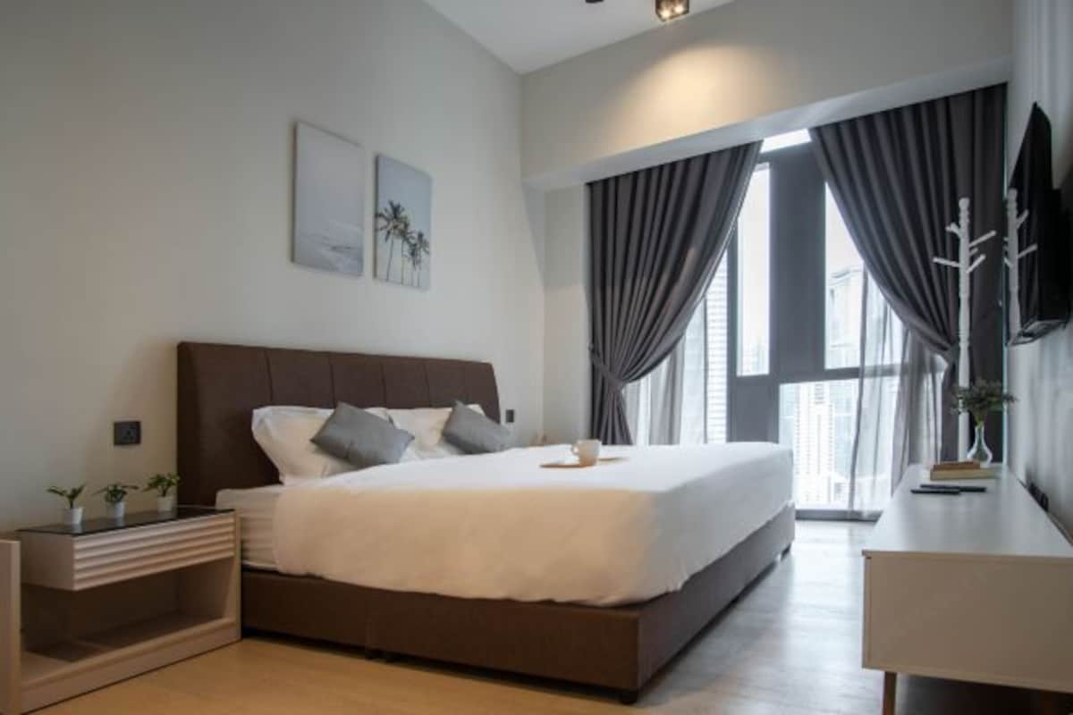 Una habitación de hotel moderna con una cama grande, una mesita de noche, un escritorio y una ventana con cortinas.