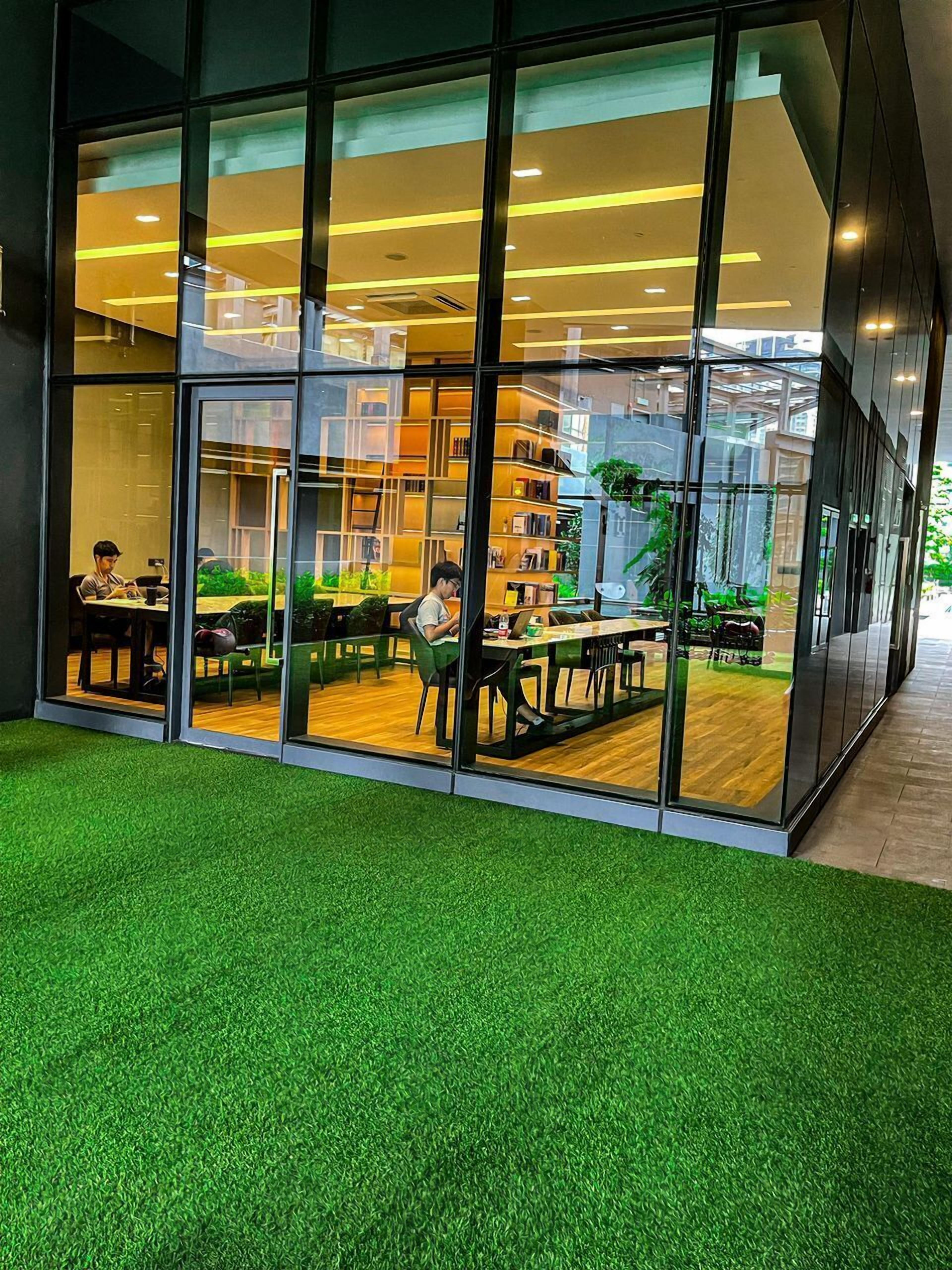 A modern library with glass walls, indoor plants, and wooden tables.
