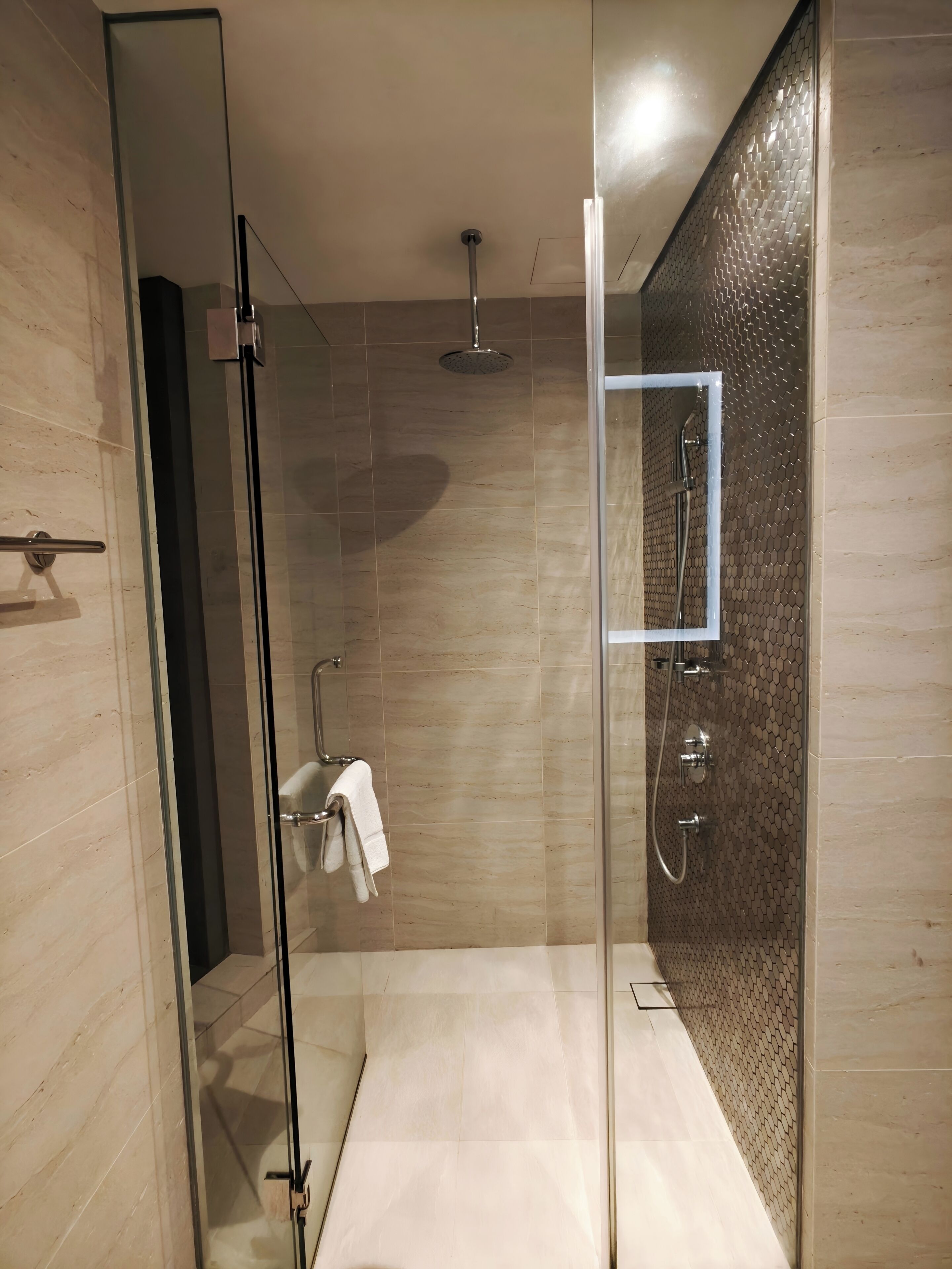 A modern shower with a glass door, a handheld showerhead, and a wall-mounted faucet.