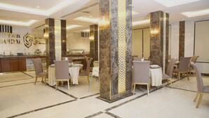 A hotel lobby with marble columns, a reception desk, and dining area with chairs and tables. - Vandal Hotels (Jizan)