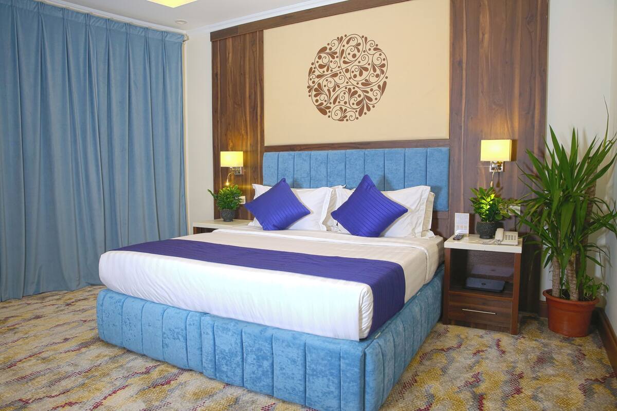 A hotel room with a large bed, blue headboard, and two bedside tables with lamps and potted plants.