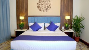 A hotel room with a large bed, two nightstands with lamps, a decorative wall piece, and two potted plants. - Vandal Hotels (Jizan)