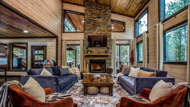 A spacious living room with a fireplace, large windows, and wooden walls. - Family Fun Cabin: Hot Tub + Game Room Retreat (Broken Bow)