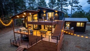 A two-story wooden cabin with a deck, outdoor seating, and a fireplace. - Family Fun Cabin: Hot Tub + Game Room Retreat (Broken Bow)