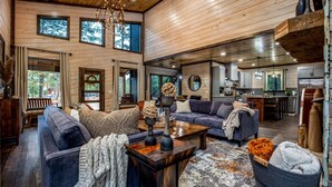 A spacious living area with a high ceiling, wooden walls, and large windows. - Family Fun Cabin: Hot Tub + Game Room Retreat (Broken Bow)
