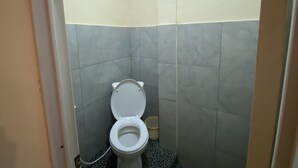 Casa de banho pequena com sanita, um contentor de lixo e paredes com azulejos.