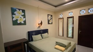 Quarto com cama, escrivaninha e mesa de cabeceira. Há luminárias fixadas na parede e uma porta com janela.