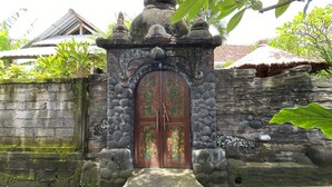 Uma entrada de pedra com porta decorativa, rodeada por um muro de pedra e vegetação.