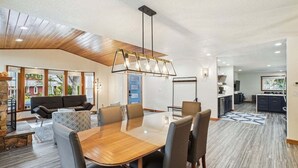 Un'ampia zona giorno con soffitto in legno, un tavolo da pranzo con sedie, un divano e una cucina sullo sfondo.