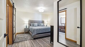 Una camera da letto con un letto, un comodino, una lampada e vista sul bagno tramite una porta.