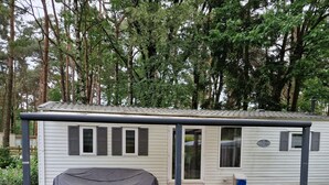 Ein kleines, eingeschossiges Mobilheim mit überdachter Terrasse, einer kleinen Holzterrasse und einem Moskitonetz-Vorraum.
