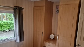 Ein Schlafzimmer mit einem Bett, einem Holzschrank, einem kleinen Schreibtisch mit Spiegel und einem Fenster mit Vorhängen.