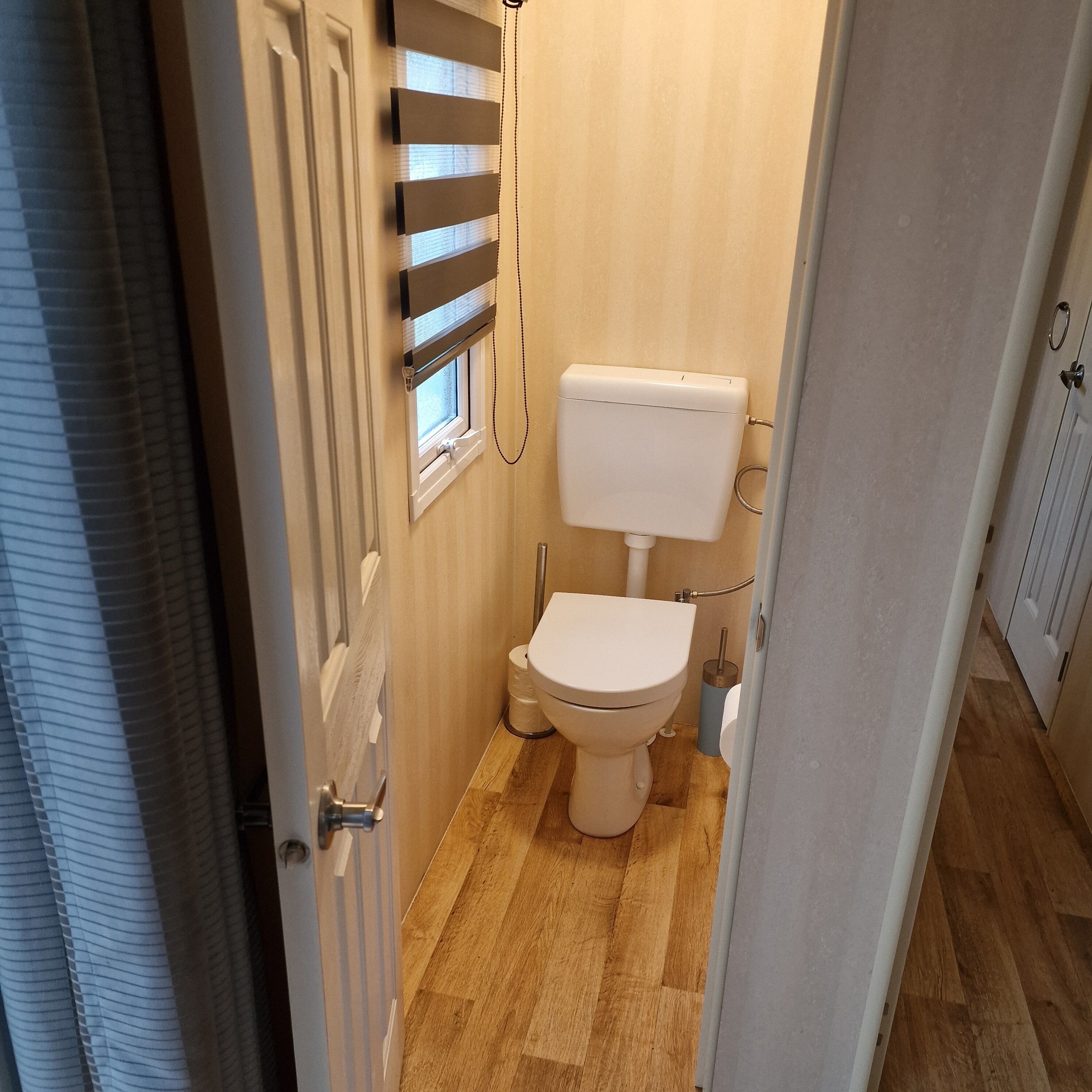 Un baño pequeño con inodoro, una ventana con persianas y suelo de madera.