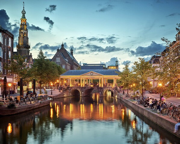 A canal with a bridge, a historic building with a tower, and a covered walkway with seating. - Leiden City Centre Terrace View Apartment in a 1750's building (Leiden)
