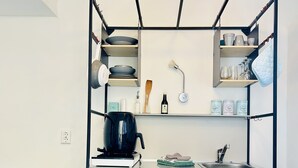 Een compact keukenhoekje met een zwart-wit kleurenschema, met een koffiezetapparaat, een spoelbak en planken met keukengerei.