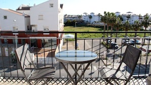 A balcony with a round table and two chairs, overlooking a parking area and buildings with palm trees.