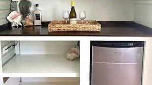 A compact kitchen with a built-in dishwasher, a wine bottle, and two glasses on a woven tray. - Watercolor a Charming Island Cottage. 3 Bedroom (Dunmore Town)