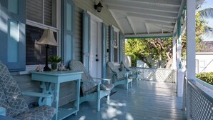 A covered porch with light blue furniture and a small table with a lamp. - Watercolor a Charming Island Cottage. 3 Bedroom (Dunmore Town)