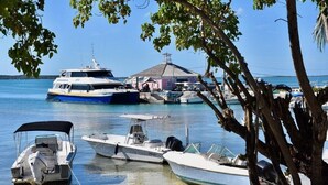 A marina with several boats docked, a small building with a thatched roof, and trees framing the scene. - Watercolor a Charming Island Cottage. 3 Bedroom (Dunmore Town)