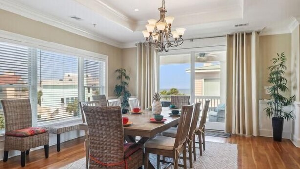 A dining area with a chandelier, wicker chairs, a wooden table, and a view through a glass door. - The Tip of Tybee Townhouse (Tybee Island)