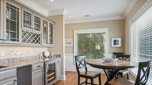 A kitchen with a round table and chairs, a window with blinds, and a door with a glass panel. - The Tip of Tybee Townhouse (Tybee Island)
