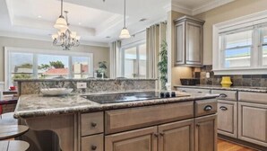 A kitchen with granite countertops, wooden cabinets, a built-in stove, and pendant lighting. - The Tip of Tybee Townhouse (Tybee Island)