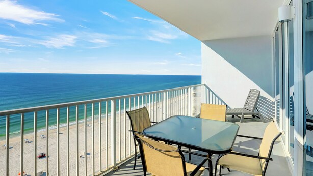 Un balcon avec une table et des chaises en verre, donnant sur une plage et l’océan.