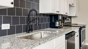 A kitchen with a granite countertop, a stainless steel sink, white cabinets, and a black backsplash. - Spacious housing for traveling professionals (Kansas City)