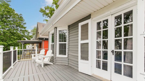A covered deck with white chairs and a red chair, a white door with multiple windows, and a grey house exterior. - Spacious housing for traveling professionals (Kansas City)