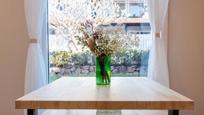 A wooden table with a green vase containing flowers, positioned in front of a window with curtains.