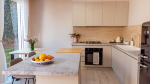 A modern kitchen with a marble countertop, a bowl of fruit, and a view of the outdoors.