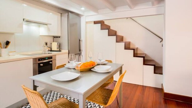 Eine moderne Küche mit weißen Schränken, einem Esstisch mit Tellern und Gläsern sowie einer Treppe mit Holzstufen.
