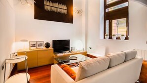 Ein modernes Wohnzimmer mit einer Couch, einem Fernseher, einem Glastisch und einem Holzschrank.