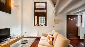 Ein modernes Wohnzimmer mit einer Couch, einem Glastisch, einem Fernseher und einem Fenster mit Jalousien.