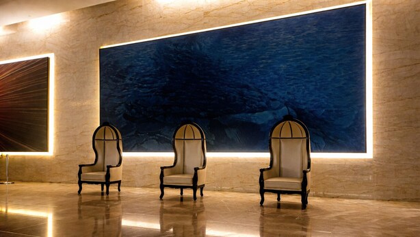 Three armchairs in a lobby with a large abstract mural on the wall.