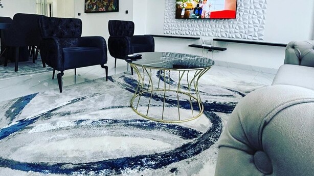 A modern living room with a flat-screen TV mounted on a textured wall, black sofas, a round coffee table, and a patterned rug. - Luxurious and cosy lodge in Dakar-Alamadies with private pool (Dakar)