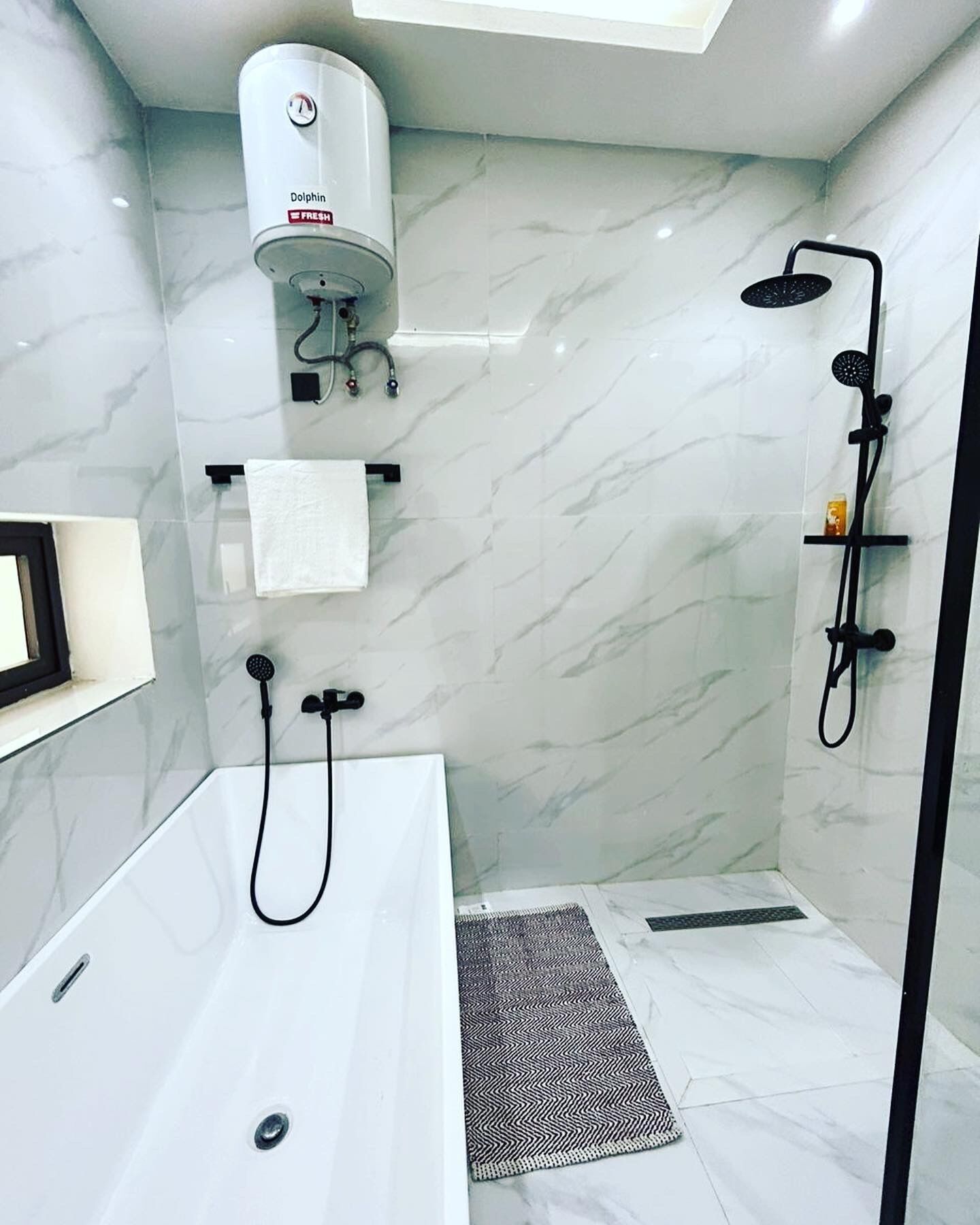 A modern bathroom with a white bathtub, a separate shower area, a towel rack, and a built-in heater.