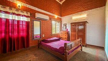 Traditional room with a wooden bed, brick wall, and a wardrobe, offering a view of lush greenery.