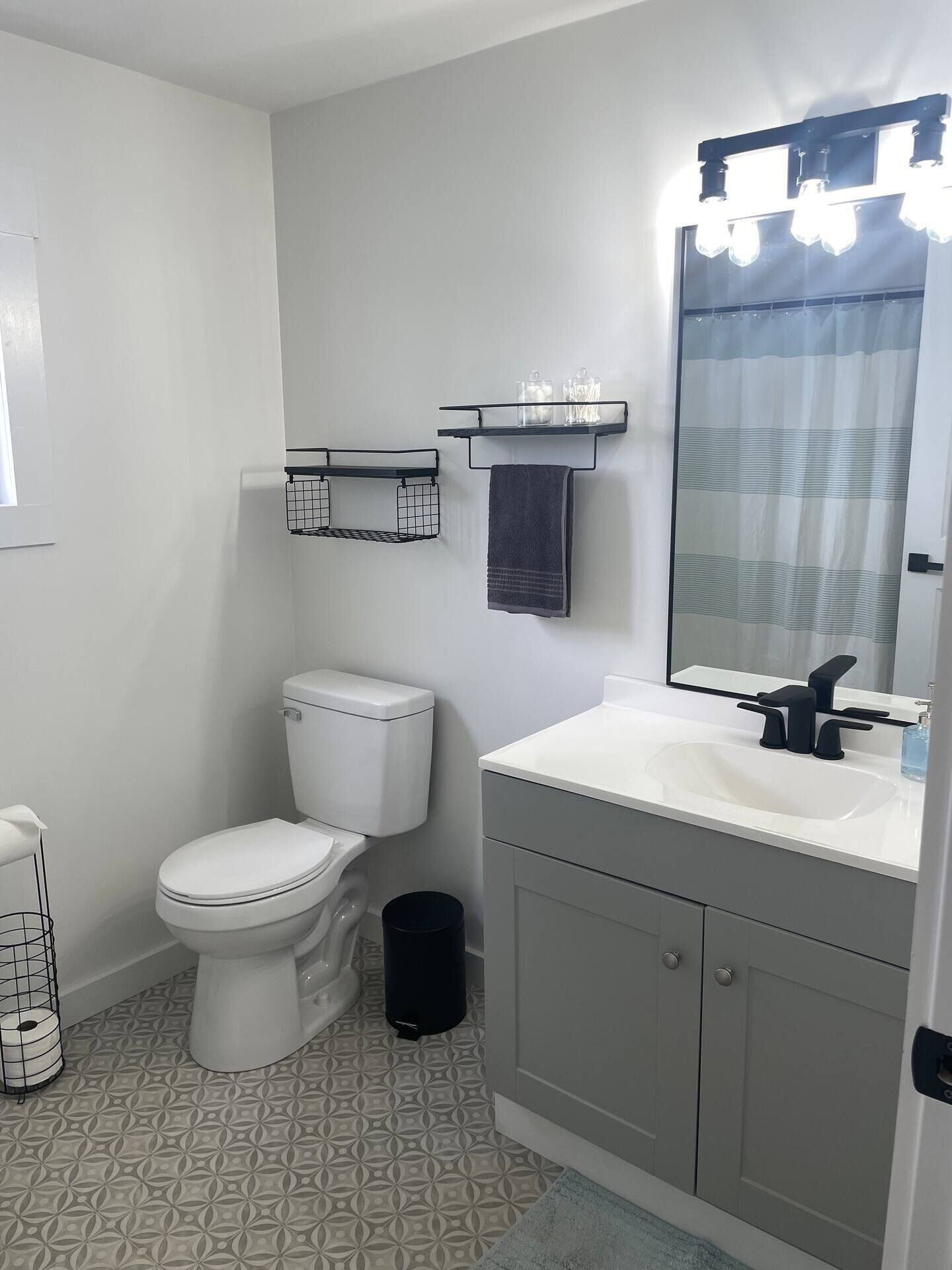 A modern bathroom with a toilet, sink, and mirror. There are towel racks and a trash can.