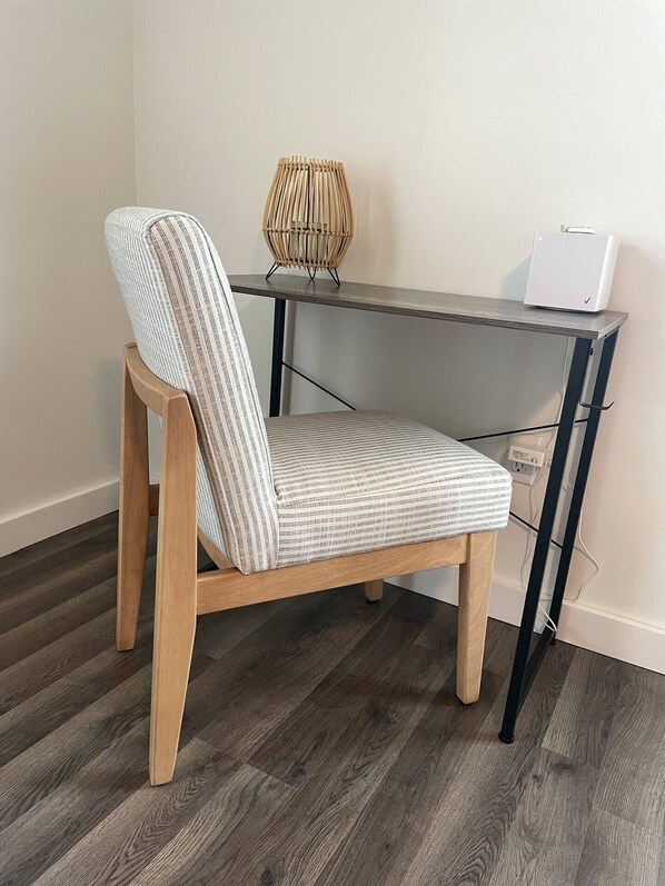 A chair with a patterned cushion, a desk with a lamp, and a white device on top.
